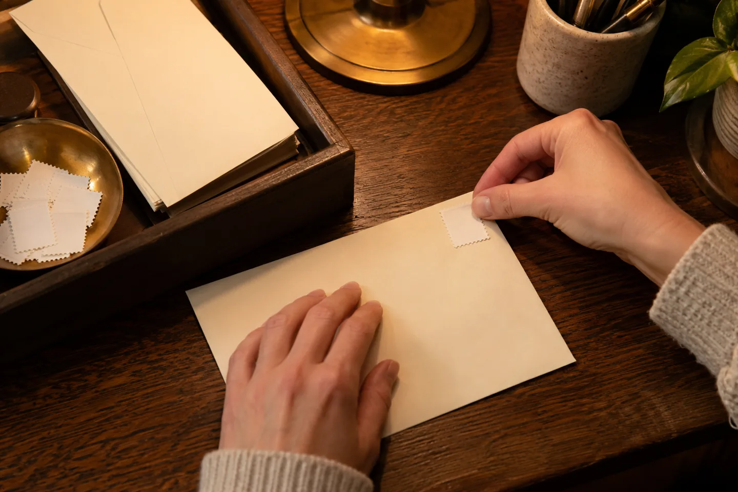 Adult hands applying a plain stamp to a blank cream envelope
