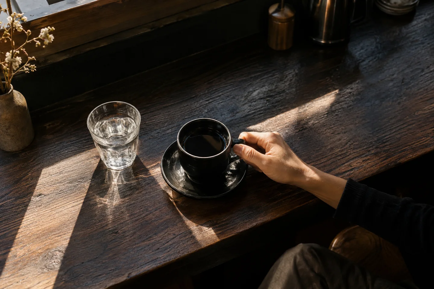 Black coffee and water sit on a cafe counter in diagonal sunlight