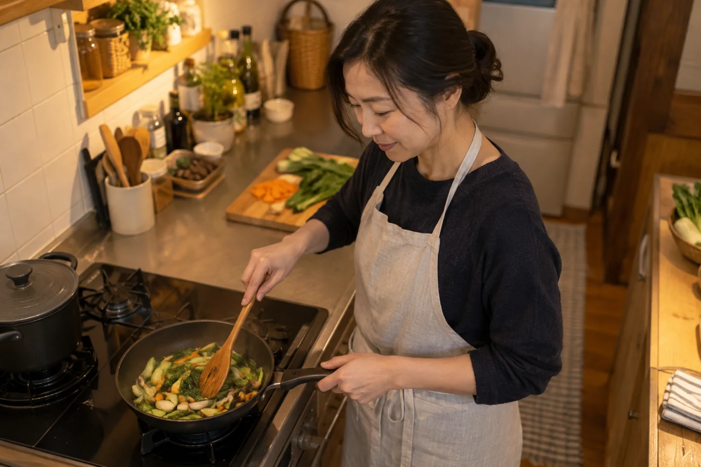 An adult stirs vegetables in a compact kitchen under warm evening light