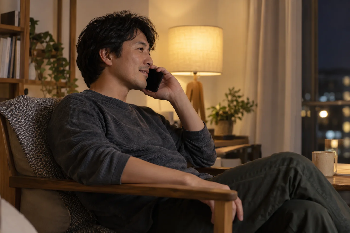 An adult holds a plain phone to an ear beside a warm evening lamp