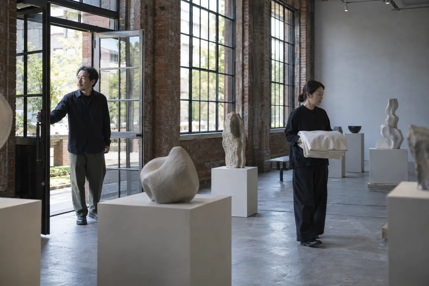 Dois adultos preparando uma exposição de esculturas numa galeria de tijolos