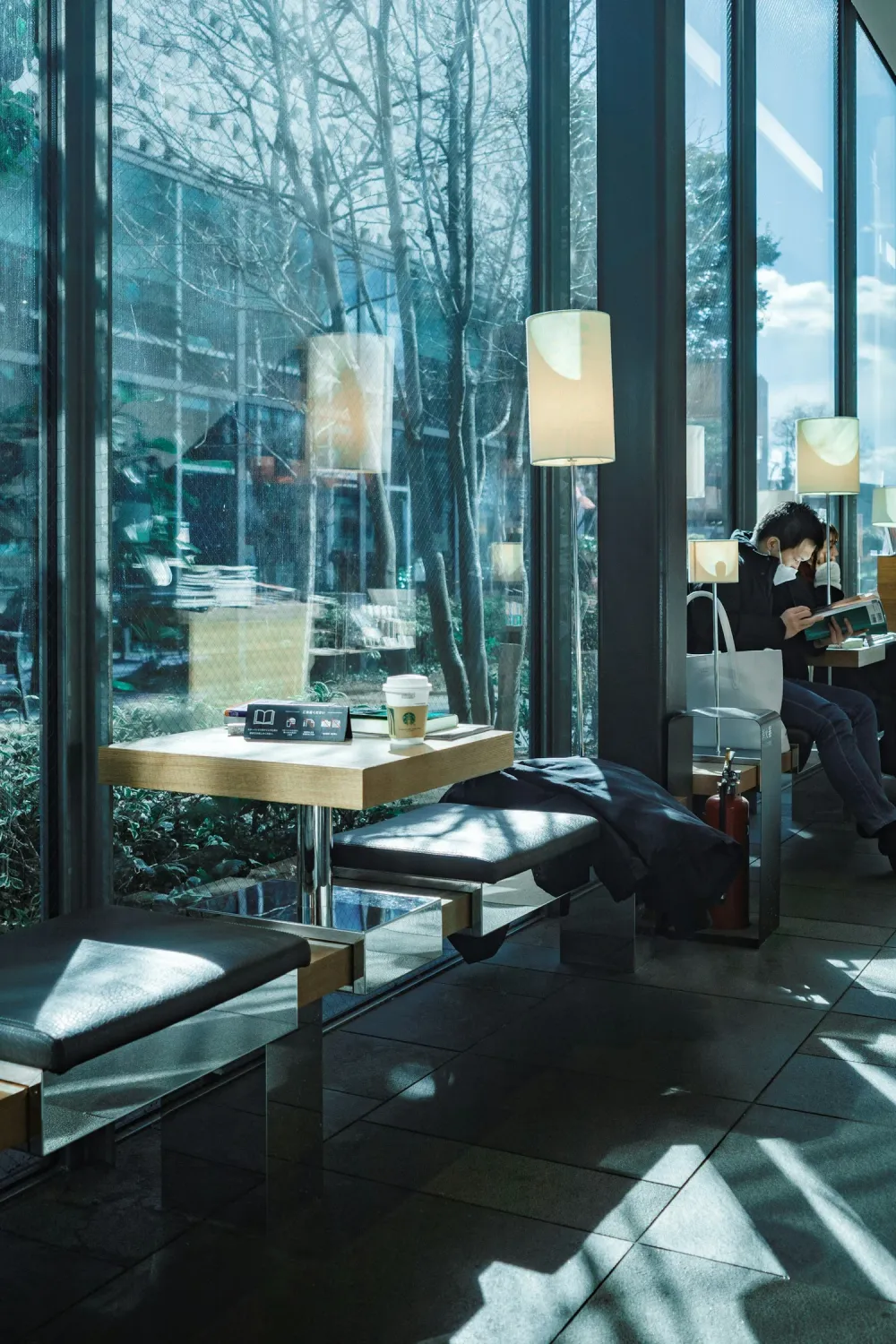 Sunlit tables and a person reading beside the large windows of a Tokyo café