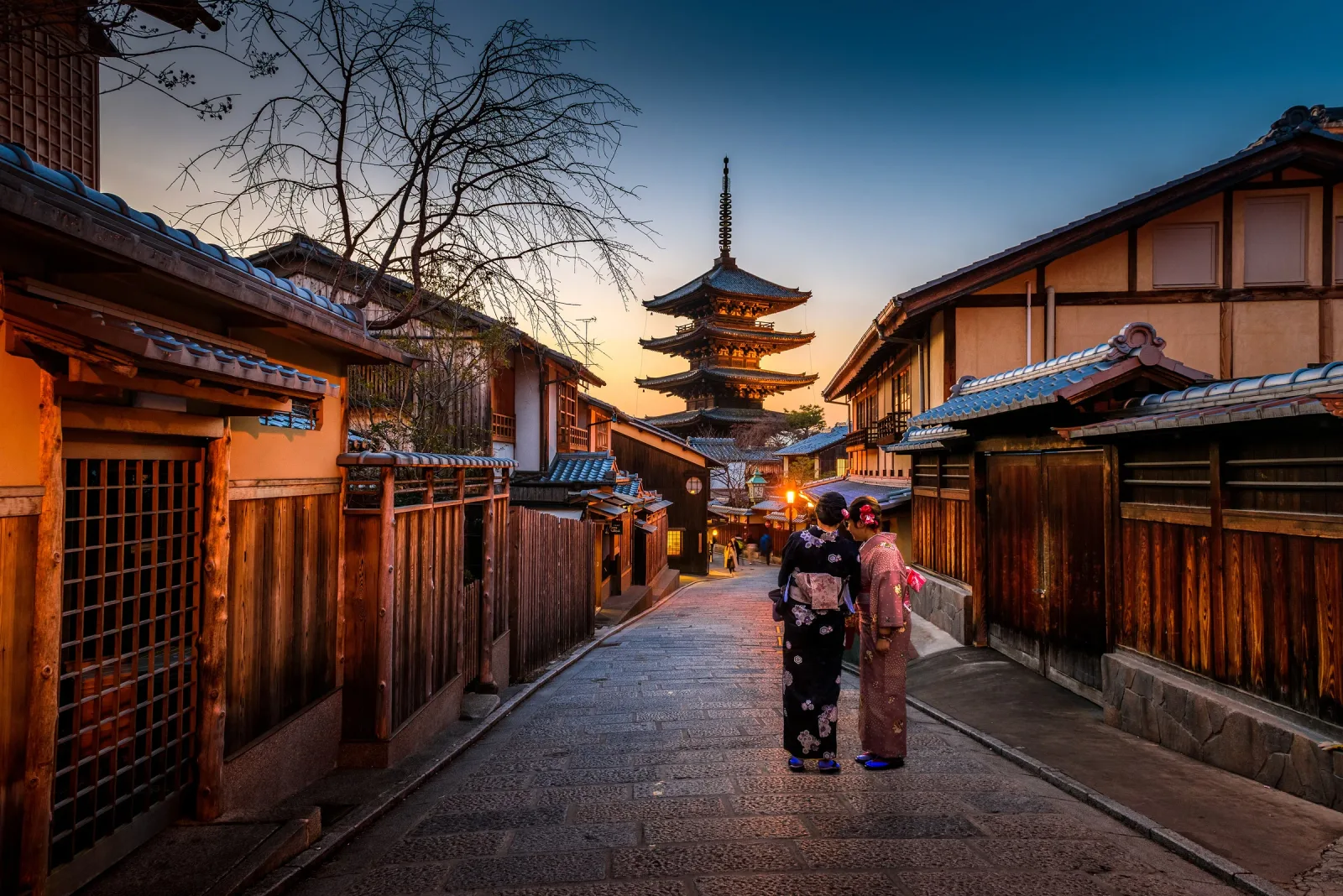 Two people walking along a traditional Kyoto street toward Yasaka Pagoda at dusk
